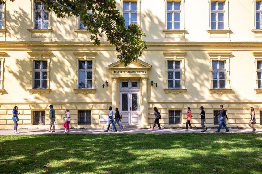 Un bâtiment à la façade jaune, avec un arbre devant et des personnes qui marchent sur le trottoir. 5