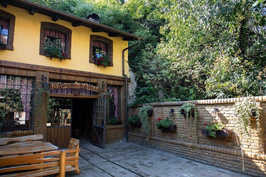 A rustic building with a yellow facade, wooden shutters, and a brick wall adorned with hanging flower baskets. 4
