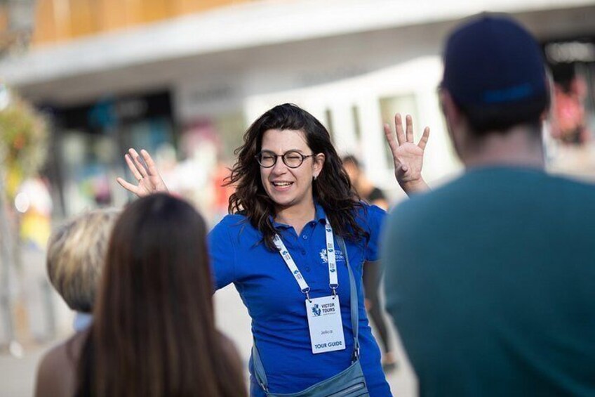 A person in a blue shirt with a lanyard, standing outdoors with raised hands. 4