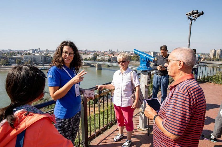 Un grupo de personas de pie sobre un puente con vista a un río, y un paisaje urbano al fondo. 1
