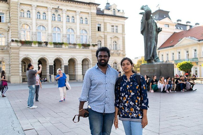 A man and a woman standing in a public square with a statue and historic buildings in the background. 5