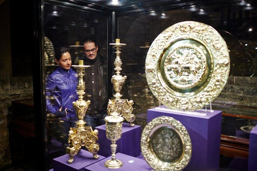 A display of ornate golden artifacts, including a large plate and several vases, in a museum setting. 2
