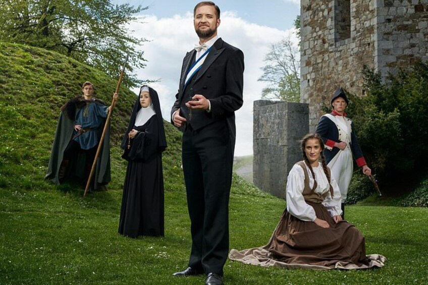 A historical reenactment scene with individuals in period costumes, a stone building, and a grassy area. 2