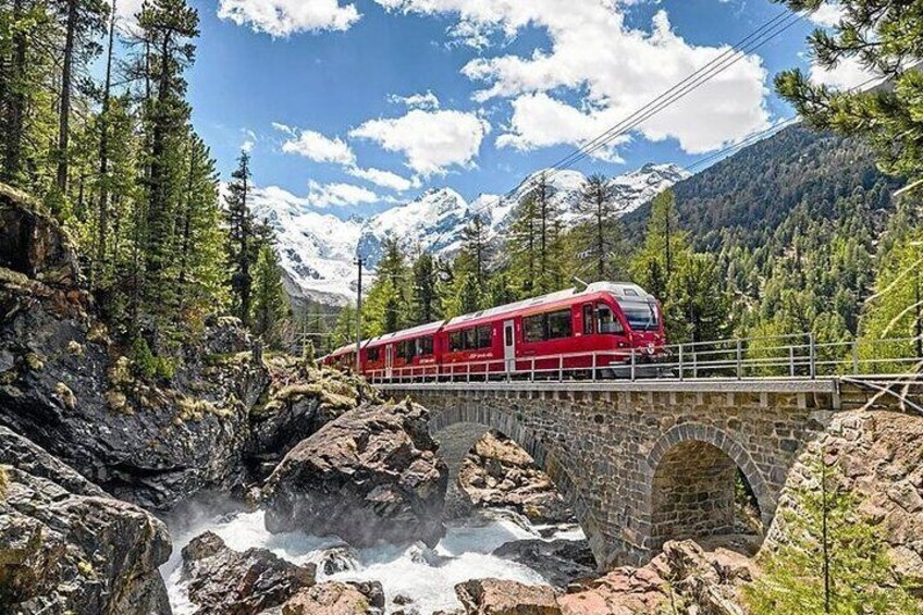 A red train crossing a stone bridge over a river in a mountainous area. 2