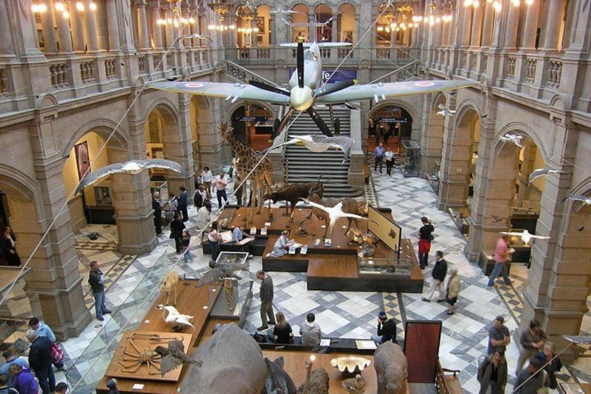 A grand hall with a large suspended sculpture, ornate architecture, and various exhibits on the floor. 2