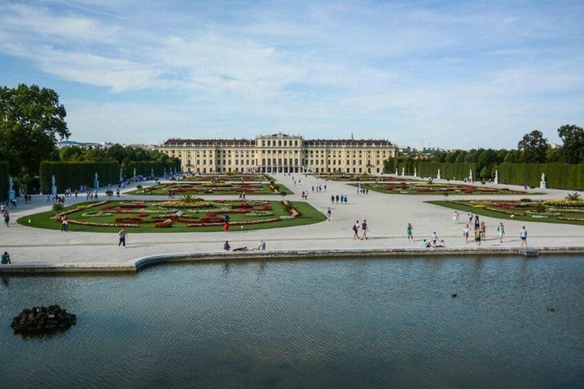 A large palace with a formal garden and a body of water in the foreground. 3