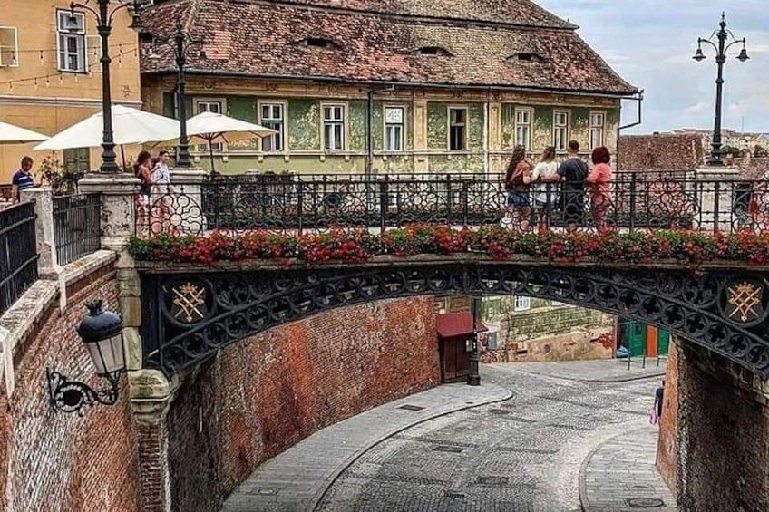 Un puente peatonal con barandillas ornamentadas, un muro de ladrillo y un edificio con techo de tejas. 2