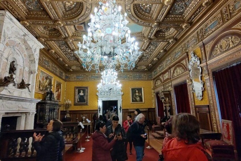 An ornate room with a large chandelier, golden ceiling, and red carpet. 3