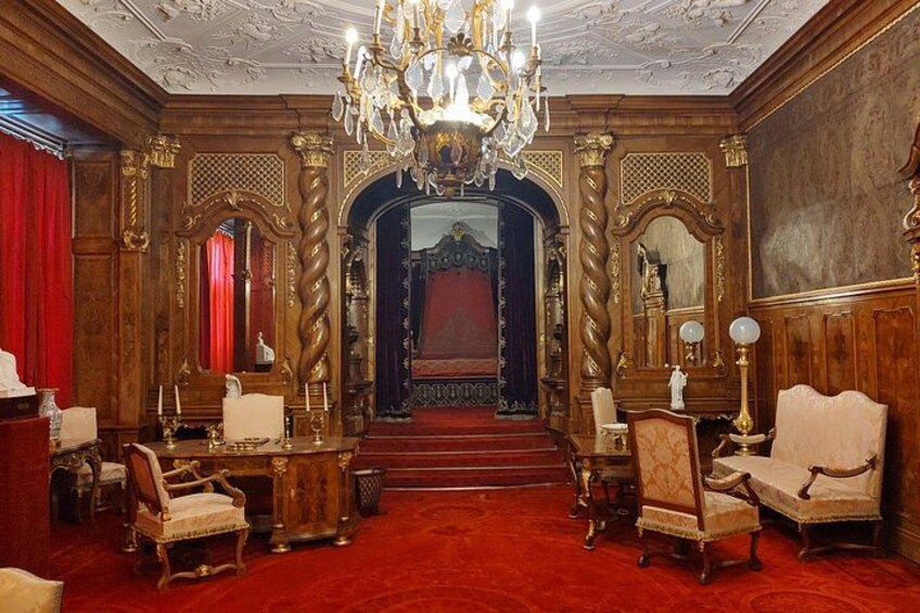 An ornate room with a red carpet, wooden furniture, and a chandelier. 5