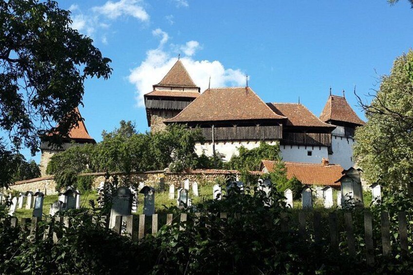 A historic building with multiple towers and a white facade, surrounded by greenery and a stone fence. 2