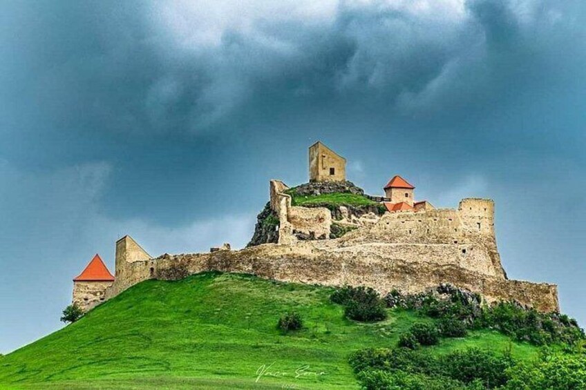 Un château perché sur une colline, avec un bâtiment à toit rouge et un mur de pierre. 4