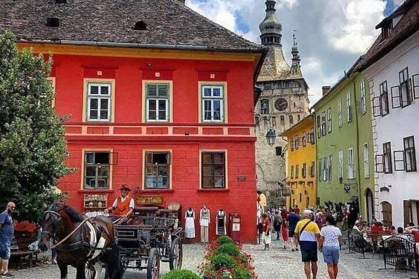 Une rue pavée bordée de bâtiments aux couleurs vives, un attelage tiré par des chevaux et une tour de l’horloge. 2
