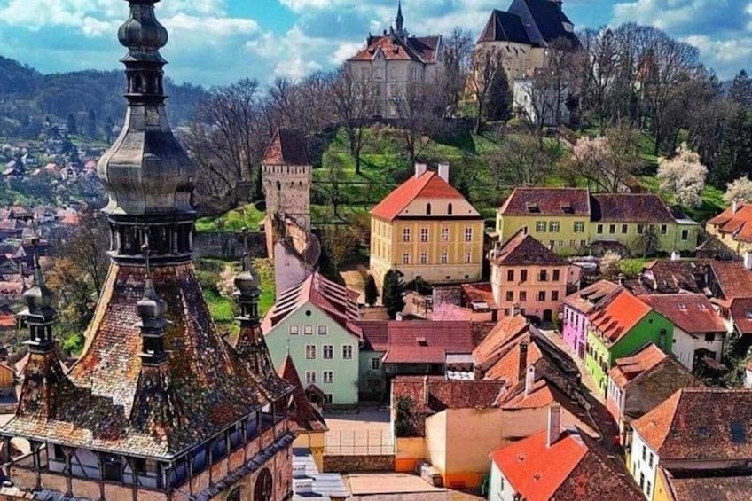 A town with colorful buildings, a prominent church tower, and a castle on a hill. 1
