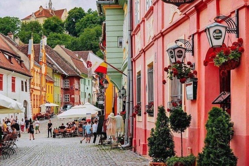 A cobblestone street lined with colorful buildings, outdoor seating, and hanging flower baskets. 5