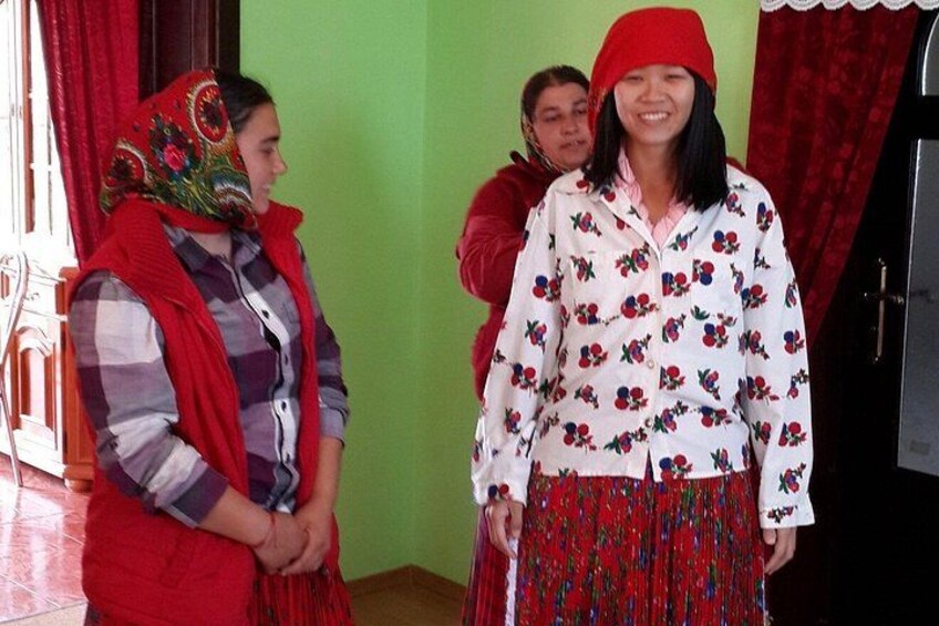Three people in a room with green walls, one wearing a red beanie and a patterned scarf, another in a red dress, and a third in a white blouse with a floral pattern. 3
