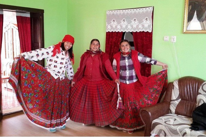 Three people in traditional red skirts and white tops, standing in a room with a green wall and a brown leather couch. 2