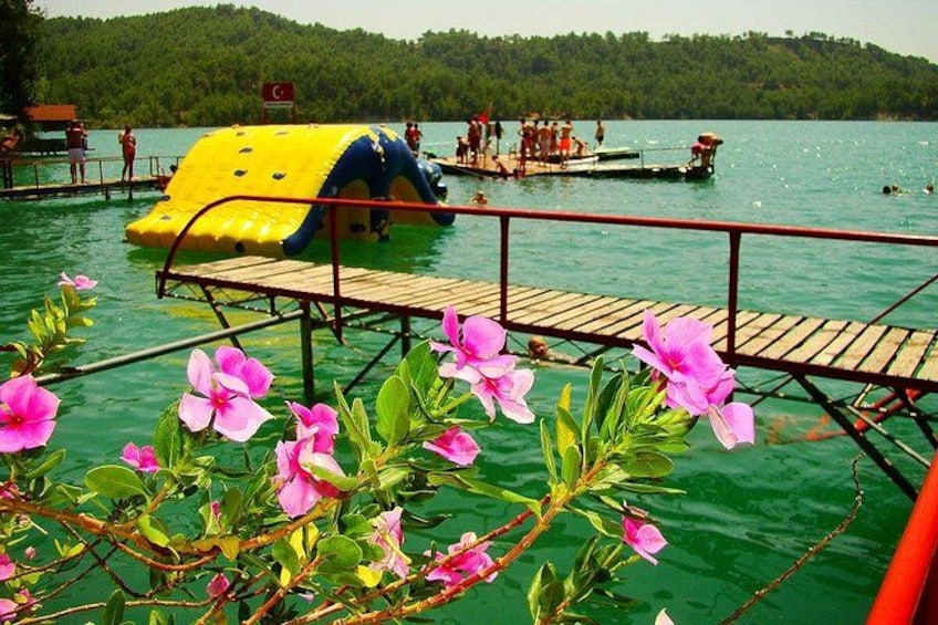 Ein Wasserpark mit einer gelben Rutsche, einem hölzernen Steg und pinkfarbenen Blumen im Vordergrund. 2