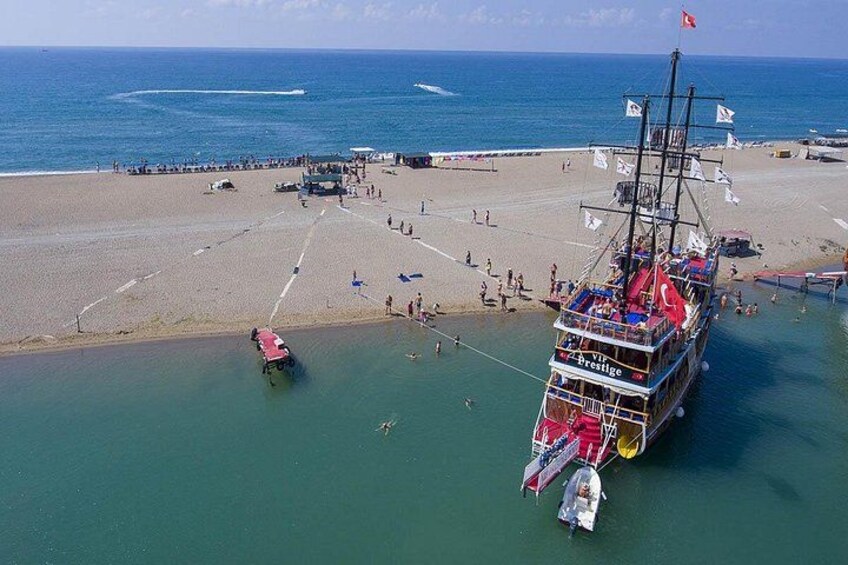 Une plage avec un grand bateau ancré près du rivage, une jetée et des personnes se promenant le long de la plage. 3
