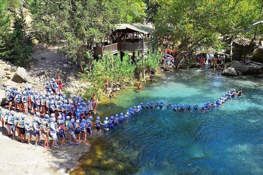 Un grupo de personas con gorras azules alineadas a orillas de un río, una estructura de madera y una zona boscosa. 3