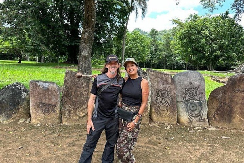 Two people standing in front of large stone slabs with carvings, in a park with trees and grass. 1