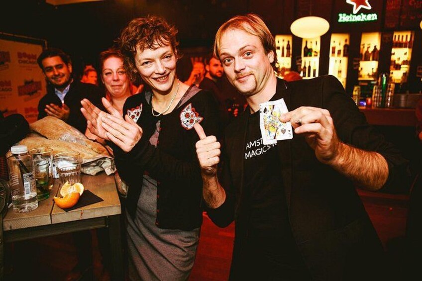 Two people performing a card trick at a bar with a Heineken sign in the background. 2
