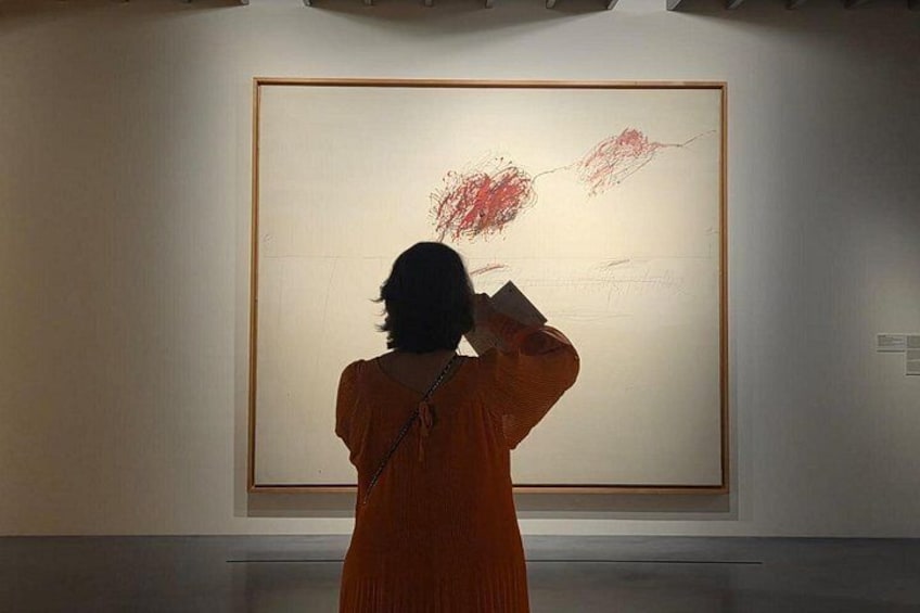 En person i en orange kjole betragter et stort abstrakt maleri i et galleri. 3