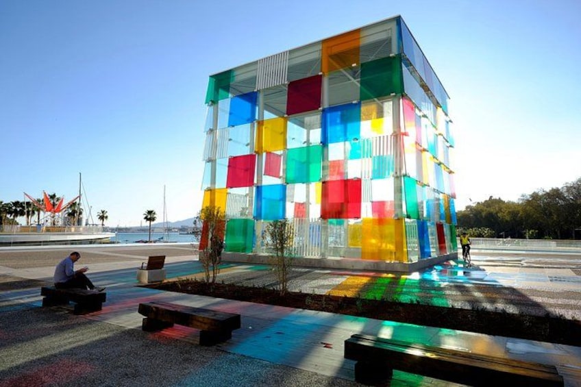 Un edificio di vetro colorato con panchine e un ciclista. 1