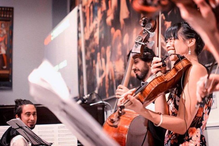 Een violist die viool speelt, een cellist met een cello, en een persoon in een zwart jack zittend aan een piano. 3