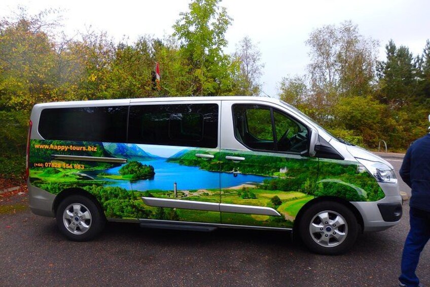 A green and white van with a scenic landscape design, parked on a road with trees in the background. 2