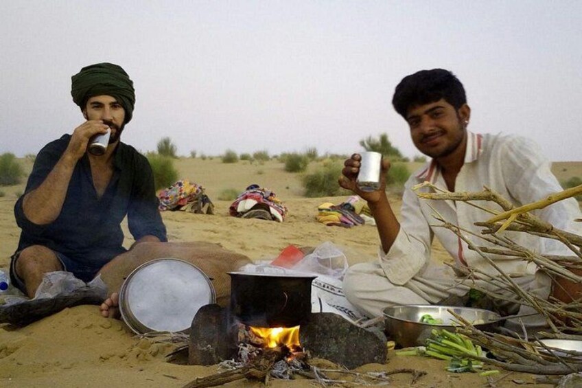 Zwei Personen sitzen am Strand und bereiten Essen über einem Lagerfeuer zu. 5