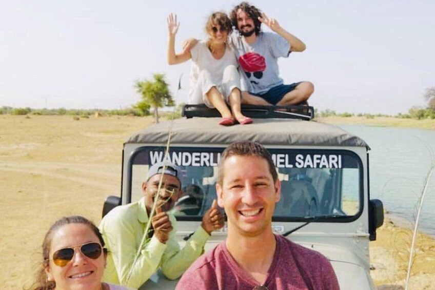 Ein Safarifahrzeug mit Personen darauf, eine trockene Landschaft und ein Gewässer im Hintergrund. 4