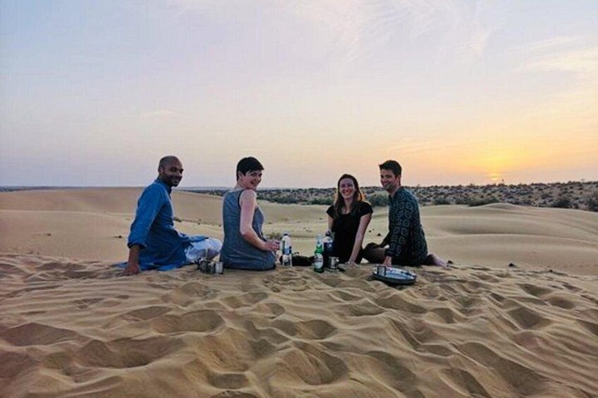 Vier Personen sitzen auf einer Düne, im Hintergrund ein Sonnenuntergang. 3