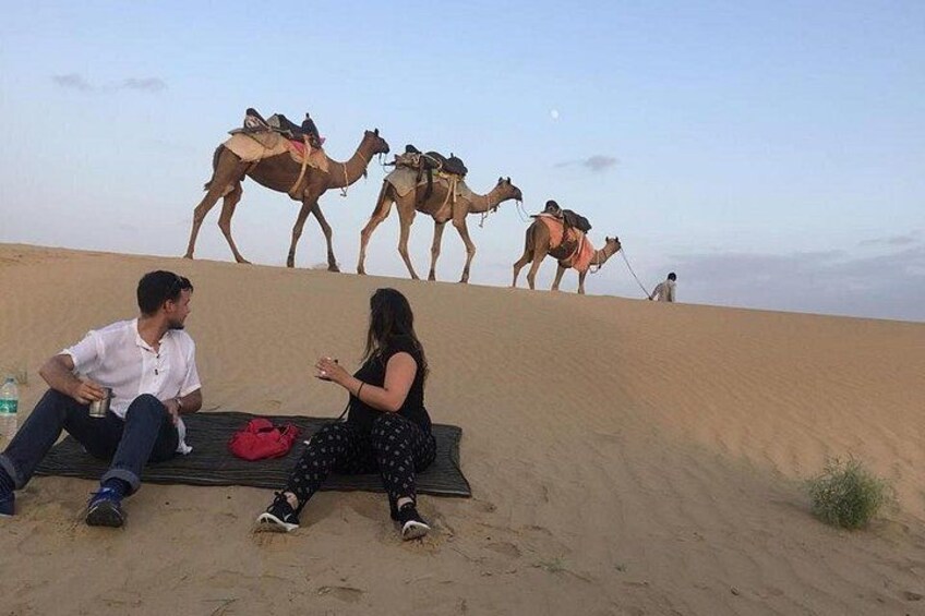 Een woestijnlandschap met kamelen en mensen die op een deken zitten. 1