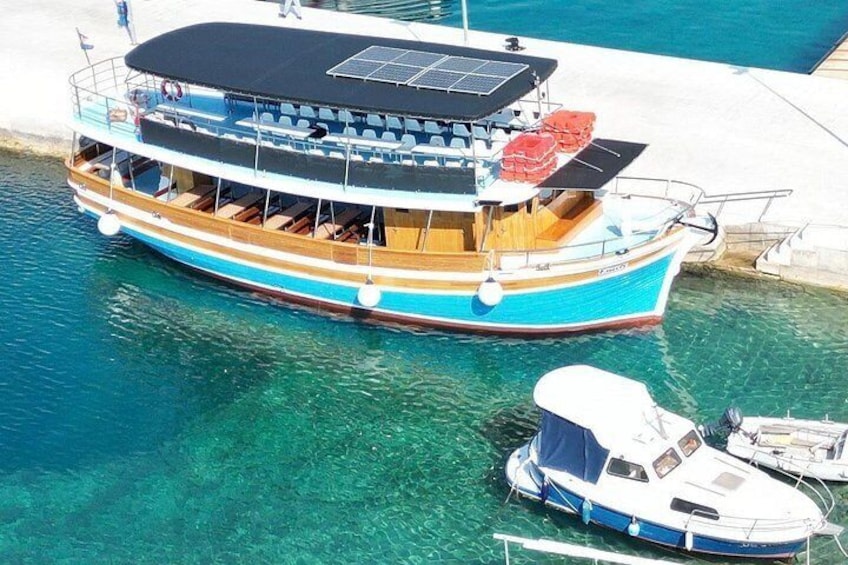A large boat with a covered upper deck, anchored near a dock with clear water. 3