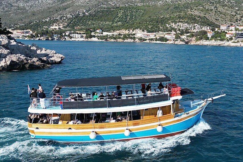 Una barca blu e gialla con passeggeri che naviga su un corpo d'acqua con rive rocciose e un paesaggio collinare sullo sfondo. 4