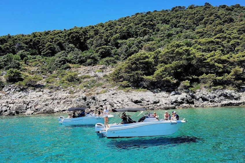 Dos barcos sobre aguas turquesas, con una costa rocosa y colinas verdes al fondo. 5
