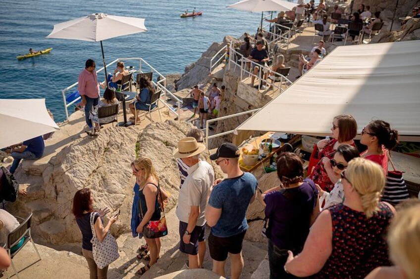 A crowded beach with people, umbrellas, and a rocky shoreline. 3