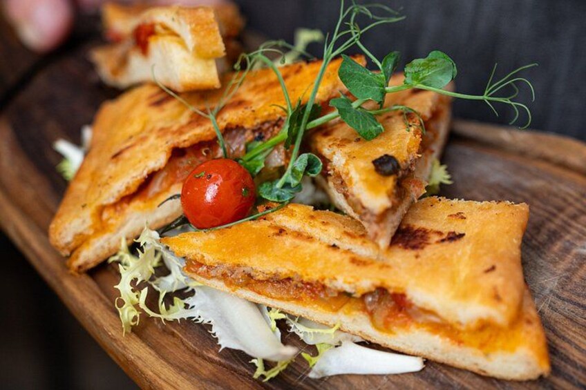 A wooden board with a grilled sandwich, garnished with greens and a cherry tomato. 2