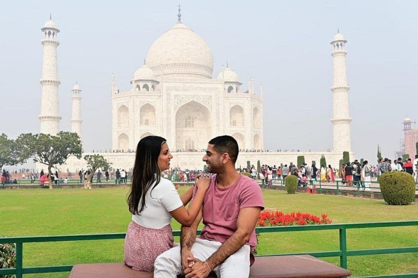 A couple sitting on a bench with the Taj Mahal in the background. 1