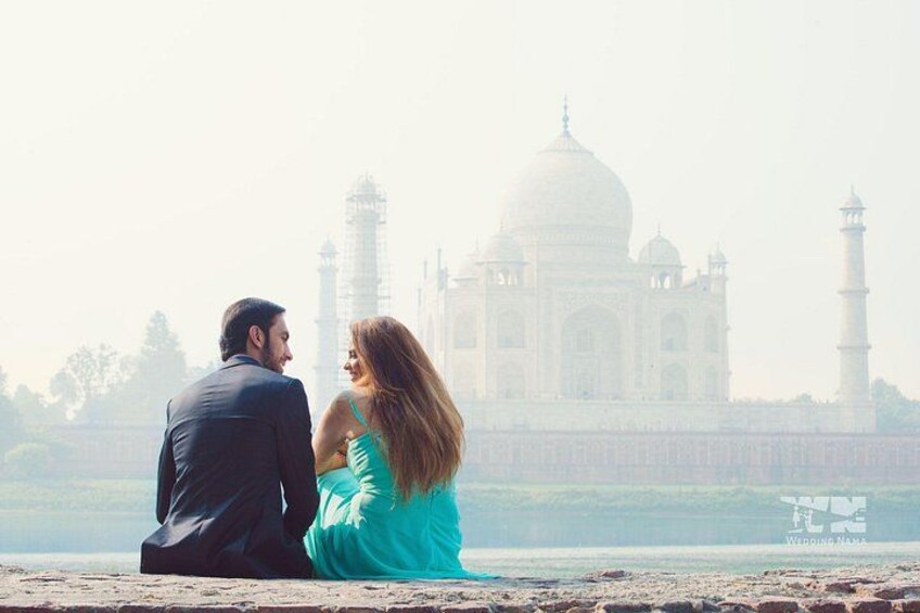A couple sitting by a body of water with the Taj Mahal in the background. 4