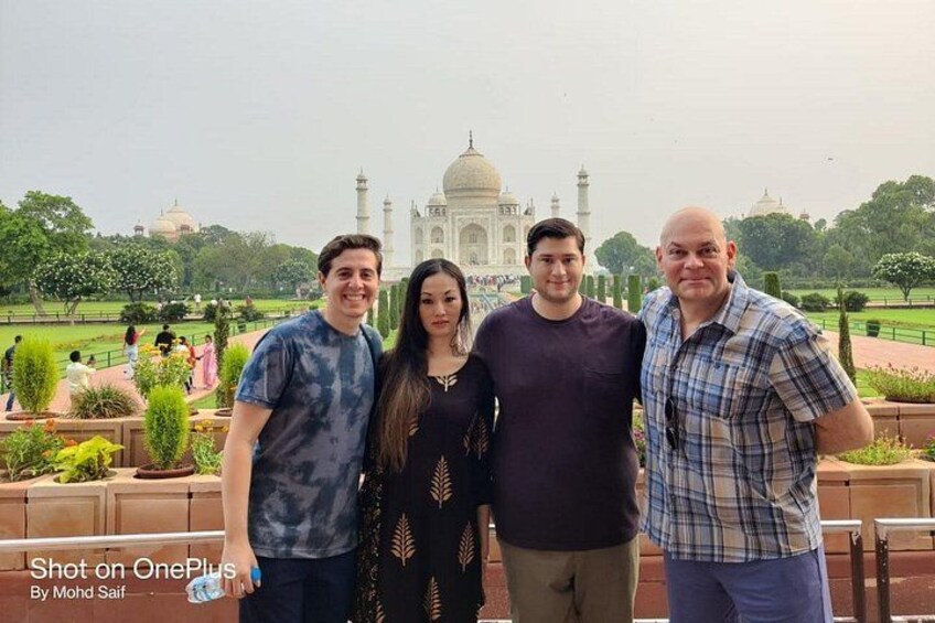 Four people standing in front of the Taj Mahal with a garden and visitors in the background. 5