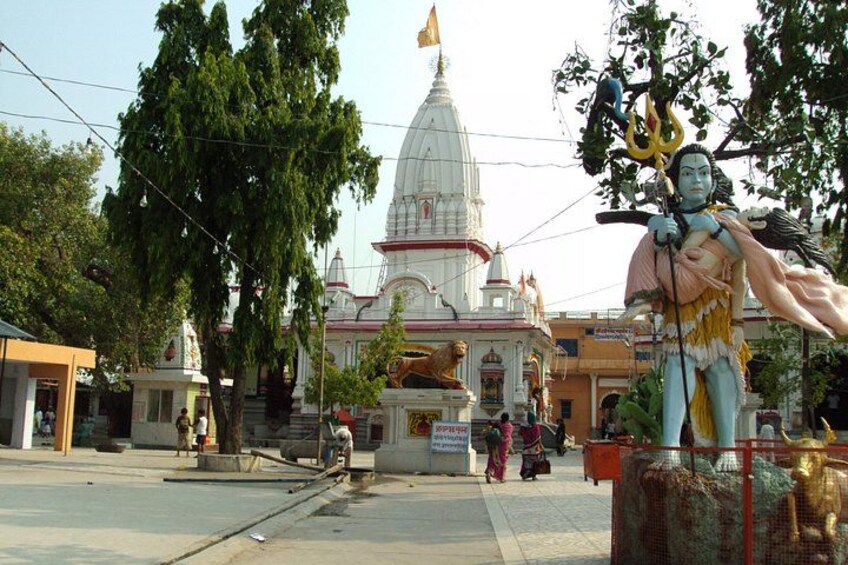 A temple with a large statue in the foreground, a white dome structure in the background, and a few people walking around. 4