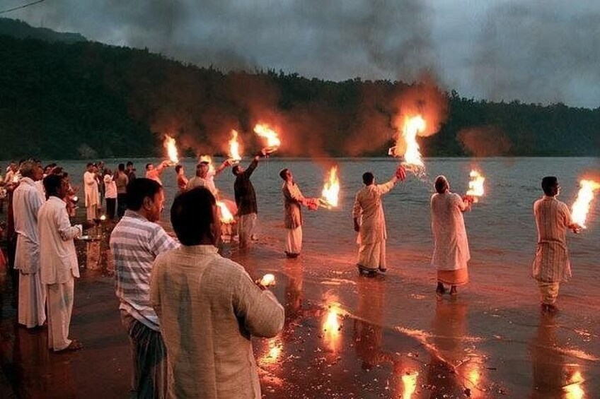 A group of people holding torches by a lake at dusk. 5