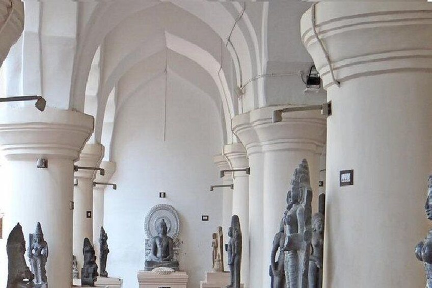 A series of statues in a gallery with high ceilings and arched columns. 2