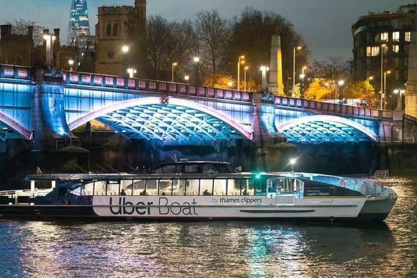 Un bateau arborant le logo « Uber Boat » navigue sur une rivière, sous un pont illuminé. 3