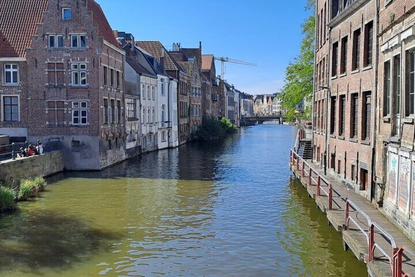 Een gracht met gebouwen aan weerszijden, een brug in de verte en een rode balustrade langs de waterlijn. 1