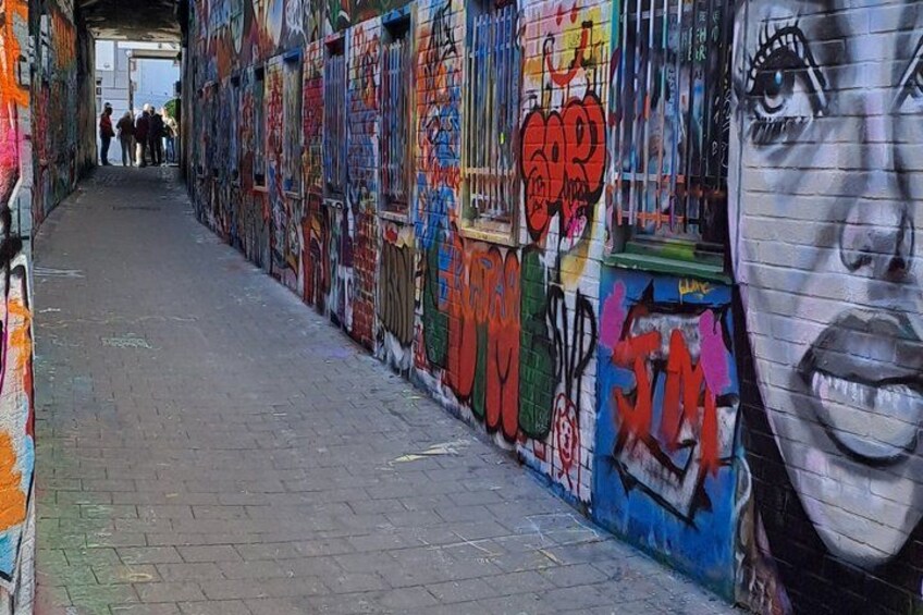 Een smalle steeg met kleurrijke graffiti op de muren en een grote muurschildering van een vrouwenportret. 4