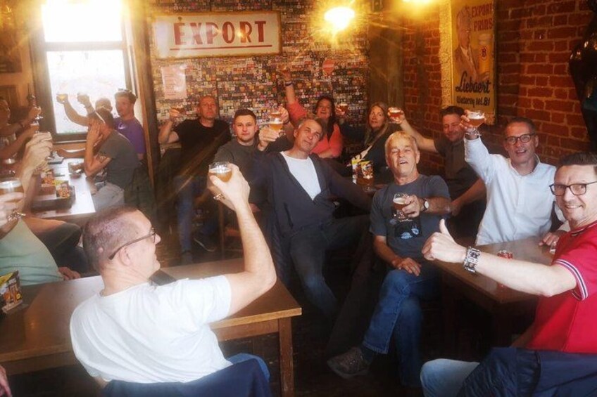 Een groep mensen proost in een bar, met een bordje waarop 'EXPORT' staat in de achtergrond. 5