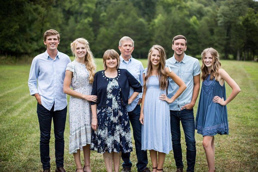 A group of people standing in a grassy field with trees in the background. 4