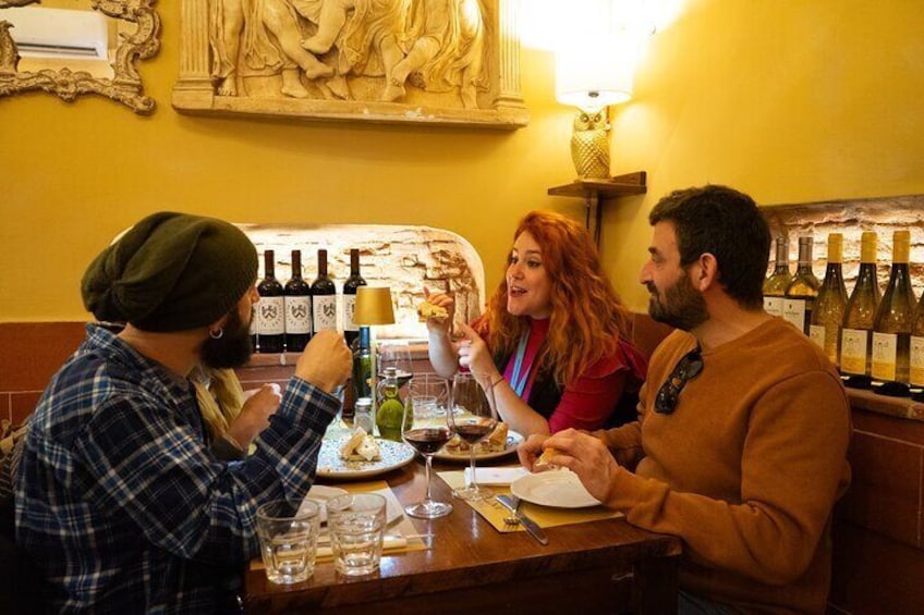 Three people dining at a restaurant with wine bottles on the wall. 3